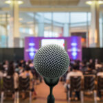 Microphone over the Abstract blurred photo of conference hall or seminar room with Speakers on the stage and attendee background, Business meeting concept